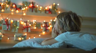Slowmotion bir yatak üzerinde asılı bir geliş takvimi bakarak küçük bir çocuk çekim Noel ışıkları ile hafifletmek. Noel ve yeni yıl konsepti için hazırlanıyor. Advent takvim kavramı