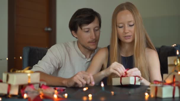 Filme lento de uma jovem mulher e homem pai e mãe presentes envoltório. Presentes embrulhados em papel artesanal com uma fita vermelha e dourada para o Natal ou ano novo. Os pais fazem um calendário de advento para — Vídeo de Stock