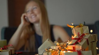 Genç bir kadın hediyelerle cep telefonuyla konuşur. Present Noel veya yeni yıl için kırmızı ve altın kurdele ile Craft kağıt sarılmış. Odak bir hediyeler üzerinde