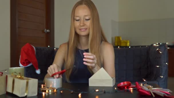 Een jonge vrouw verpakking presenteert. Aanwezig verpakt in ambachtelijke papier met een rood en goud lint voor Kerstmis of Nieuwjaar. Vrouw maakt een adventkalender voor haar kinderen — Stockvideo