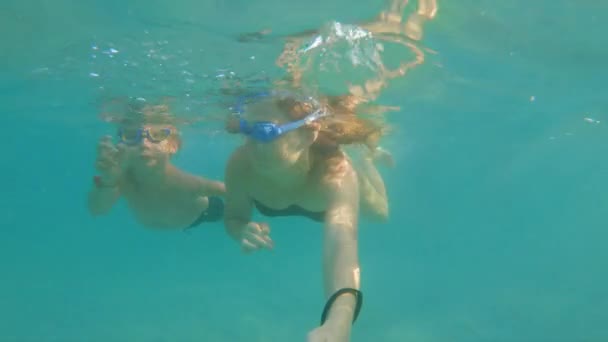 Медленная подводная съемка женщины и ее маленького сына, веселящихся в синем море — стоковое видео