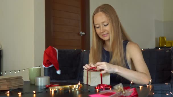 Eine junge Frau packt Geschenke ein. Geschenk eingewickelt in Bastelpapier mit einem rot-goldenen Band für Weihnachten oder Neujahr. Frau bastelt Adventskalender für ihre Kinder