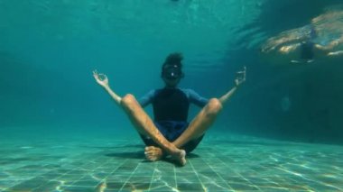 Bir yoga genç bir adamın Slowmotion sualtı çekim bir yüzme havuzunun dibinde meditasyon poz. Yakınlarda yüzerken küçük bir çocuk tarafından rahatsız oldu. tam dekolmanı imkansız kavramı