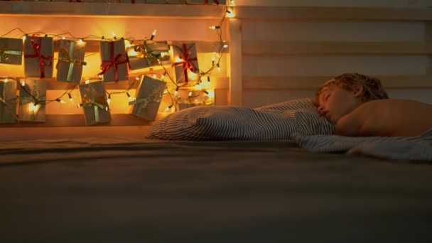 egy kisfiú alszik az ágyában egy Adventi naptár világosítani a karácsonyi fények ragyog a hátán ágya. Felkészülnek a karácsonyi és újévi koncepció. Adventi naptár koncepció