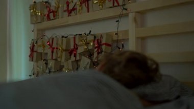küçük bir çocuk yatakta bir geliş takvimi ile uyku Noel ışıkları ile hafifletmek onun yatağın bir arka parlar. Noel ve yeni yıl konsepti için hazırlanıyor. Advent takvim kavramı