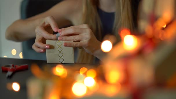 Uma jovem mulher a empacotar presentes. Presente embrulhado em papel artesanal com uma fita vermelha e dourada para o Natal ou ano novo. Mulher faz um calendário de advento para seus filhos — Vídeo de Stock