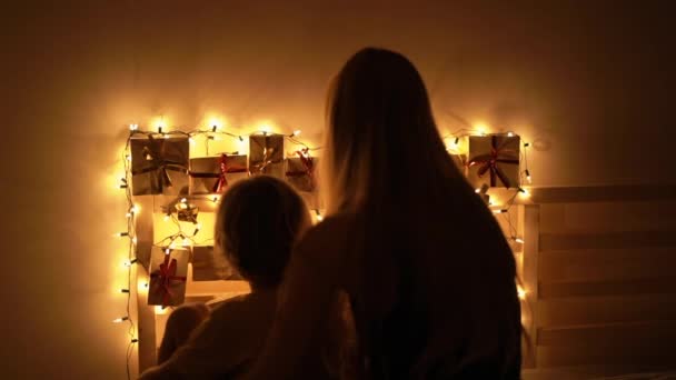 Slowmotion close-up tiro de uma mãe e seu filho pequeno olhar para um calendário de advento pendurado em uma cama iluminar com luzes de Natal. Preparando-se para o Natal e Ano Novo conceito. Calendário do Advento — Vídeo de Stock