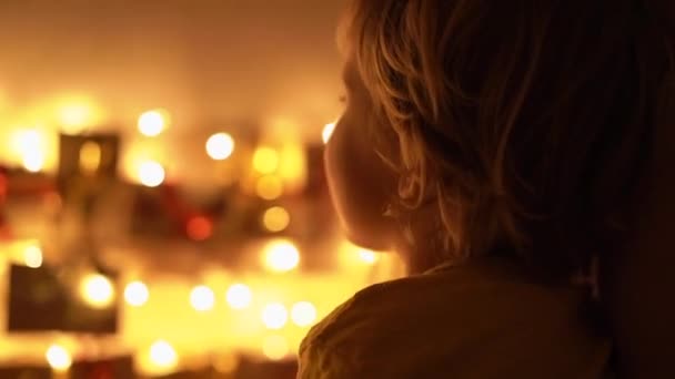 어머니와 그녀의 작은 아들의 슬로우 모션 클로즈업 샷은 크리스마스 조명으로 밝게 침대에 매달려 출현 달력을 보고. 크리스마스와 새해 개념에 대한 준비. 강림절 달력 — 비디오
