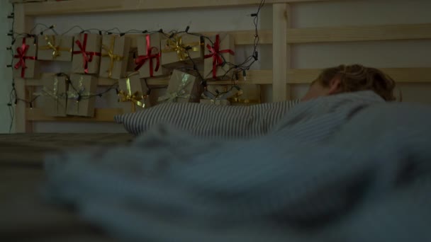 Een jongetje dat in zijn bed slaapt met een adventkalender verlicht met kerstverlichting schijnt op een achterkant van zijn bed. Klaar voor het kerst-en Nieuwjaars concept. Adventkalender concept — Stockvideo