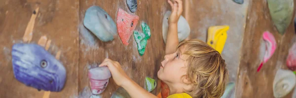 Kleiner Junge klettert in Spezialstiefeln eine Felswand hinauf. Banner für Innenräume, langes Format — Stockfoto
