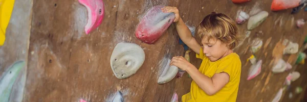 Kleiner Junge klettert in Spezialstiefeln eine Felswand hinauf. Banner für Innenräume, langes Format — Stockfoto