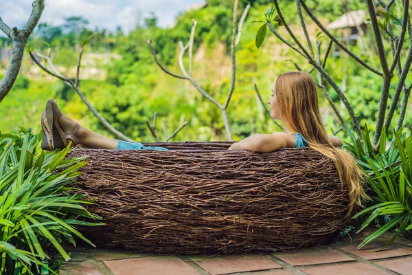 Bali trend, straw nests everywhere. Young tourist enjoying her travel around Bali island, Indonesia. Making a stop on a beautiful hill. Photo in a straw nest, natural environment. Lifestyle