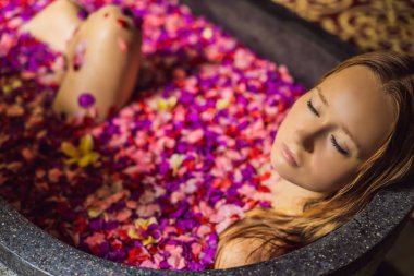 Tropik çiçekler ve aroma yağları yaprakları ile banyoda Çekici Genç kadın. Cilt gençleştirme için spa tedavileri. Spa salonunda çekici kadın. Kız çiçek yaprakları ile küvette rahatlatıcı. Lüks