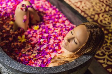 Tropik çiçekler ve aroma yağları yaprakları ile banyoda Çekici Genç kadın. Cilt gençleştirme için spa tedavileri. Spa salonunda çekici kadın. Kız çiçek yaprakları ile küvette rahatlatıcı. Lüks