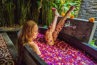 Tropik çiçekler ve aroma yağları yaprakları ile banyoda Çekici Genç kadın. Cilt gençleştirme için spa tedavileri. Spa salonunda çekici kadın. Kız çiçek yaprakları ile küvette rahatlatıcı. Lüks