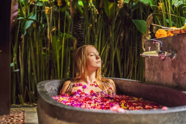 Atrakcyjna młoda kobieta w kąpieli z płatkami kwiatów tropikalnych i olejów aromatycznych. Zabiegi spa na odmodowanie skóry. Intrygująca Kobieta w salonie spa. Dziewczyna relaksująca w wannie z płatkami kwiatów. Luksusowe — Zdjęcie stockowe