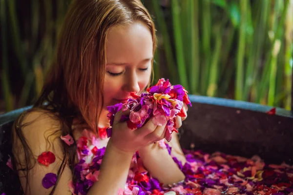 Mulher jovem atraente em banho com pétalas de flores tropicais e óleos de aroma. Tratamentos de spa para rejuvenescimento da pele. Uma mulher sedutora no salão de Spa. Menina relaxante na banheira com pétalas de flores. Luxo — Fotografia de Stock