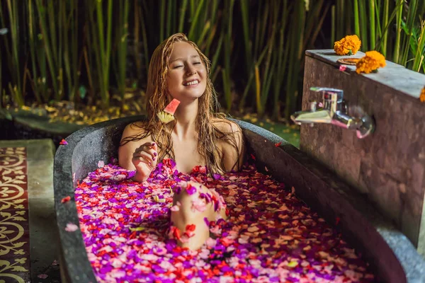 Привлекательная молодая женщина в ванной с лепестками тропических цветов и ароматическими маслами. Спа-процедуры для омоложения кожи. Очаровательная женщина в Спа салоне. Девушка отдыхает в ванной с лепестками цветов. Роскошь — стоковое фото