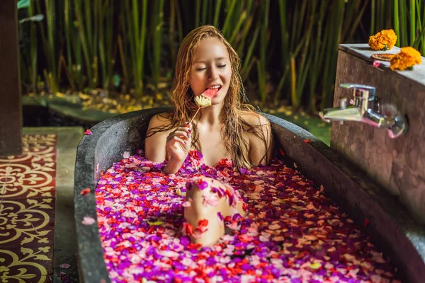 Mulher jovem atraente em banho com pétalas de flores tropicais e óleos de aroma. Tratamentos de spa para rejuvenescimento da pele. Uma mulher sedutora no salão de Spa. Menina relaxante na banheira com pétalas de flores. Luxo — Fotografia de Stock