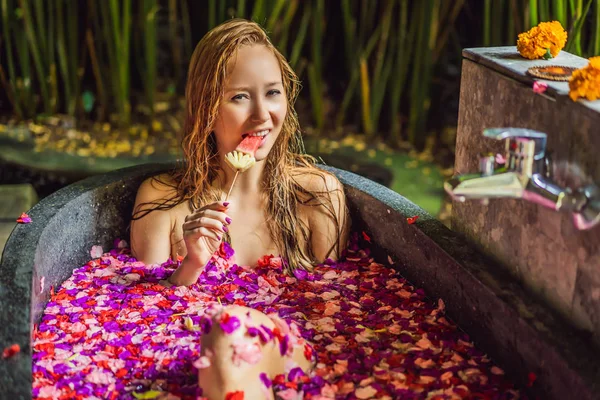 Mulher jovem atraente em banho com pétalas de flores tropicais e óleos de aroma. Tratamentos de spa para rejuvenescimento da pele. Uma mulher sedutora no salão de Spa. Menina relaxante na banheira com pétalas de flores. Luxo — Fotografia de Stock