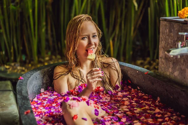 Aantrekkelijke jonge vrouw in Bad met bloemblaadjes van tropische bloemen en aroma oliën. Spabehandelingen voor huidverjonging. Verleidelijke vrouw in Spa Salon. Meisje ontspannen in Bad met bloemblaadjes. Luxe — Stockfoto