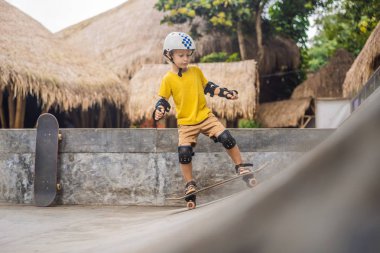 Kasklı ve dizlikli atletik çocuk kaykay yapmayı kaykay parkında öğreniyor. Çocuk eğitimi, spor