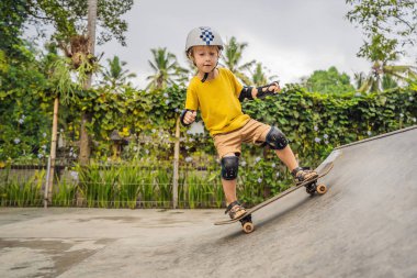 Kasklı ve dizlikli atletik çocuk kaykay yapmayı kaykay parkında öğreniyor. Çocuk eğitimi, spor