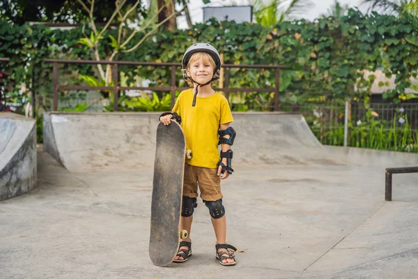 Kasklı ve dizlikli atletik çocuk kaykay yapmayı kaykay parkında öğreniyor. Çocuk eğitimi, spor