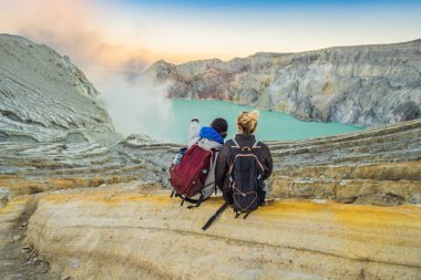 Genç turist adam ve kadın Endonezya dili üzerinde Ijen yanardağ veya Kawah Ijen krater kenarında oturup. Dünyanın en büyük asit göl ve kükürt madenciliği içeren ünlü yanardağ