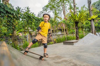 Kasklı ve dizlikli atletik çocuk kaykay yapmayı kaykay parkında öğreniyor. Çocuk eğitimi, spor