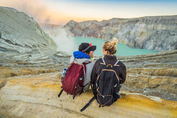 Un joven turista y una mujer se sientan al borde del cráter del volcán Ijen o Kawah Ijen en el idioma indonesio. Famoso volcán que contiene el más grande del mundo lago ácido y la minería de azufre — Foto de Stock