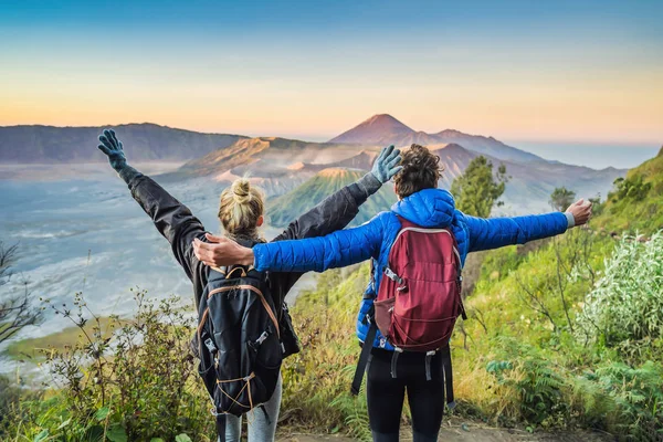 Young couple man and woman meet the sunrise at the Bromo Tengger Semeru National Park on the Java Island, Indonesia. They enjoy magnificent view on the Bromo or Gunung Bromo on Indonesian, Semeru and — Stock Photo, Image