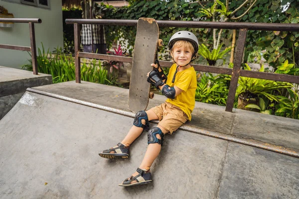 Sportlicher Junge mit Helm und Knieschoner lernt in einem Skatepark Skateboard fahren. Kindererziehung, Sport — Stockfoto