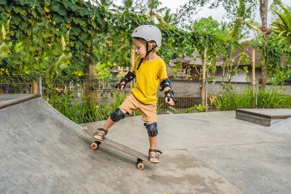 Sportlicher Junge mit Helm und Knieschoner lernt in einem Skatepark Skateboard fahren. Kindererziehung, Sport — Stockfoto