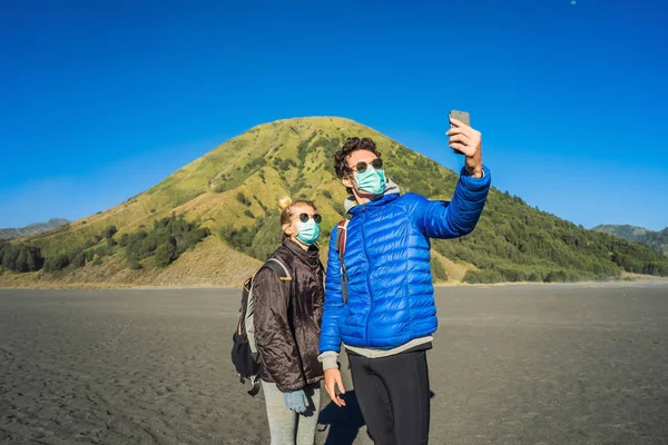 Young man and woman tourists make a selfie in the Bromo Tengger Semeru National Park on the Java Island, Indonesia. They enjoy magnificent view on the Bromo or Gunung Bromo on Indonesian, Semeru and — Stock Photo, Image