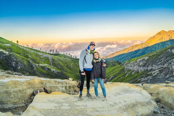 Young tourist man and woman stand at the edge of the crater of the Ijen volcano or Kawah Ijen on the Indonesian language. Famous volcano containing the biggest in the world acid lake and sulfur mining — Stock Photo, Image