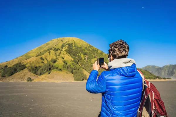 Un turista joven toma una foto del volcán Batok en su celular. Está en el Parque Nacional Bromo Tengger Semeru en la isla de Java, Indonesia. Disfruta de magníficas vistas sobre el Bromo o Gunung — Foto de Stock