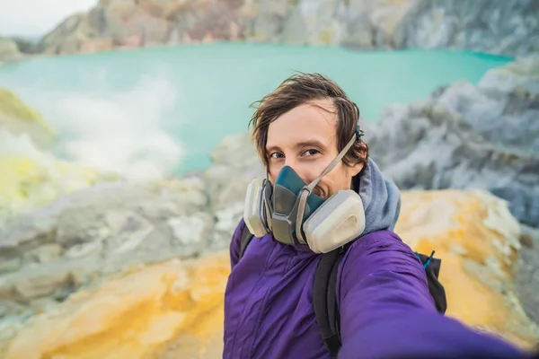 Young man tourist makes a selfie standing at the edge of the crater of the Ijen volcano or Kawah Ijen on the Indonesian language. Famous volcano containing the biggest in the world acid lake and — Stock Photo, Image