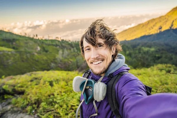 Young man tourist makes a selfie with the magnificent views on green mountains from a mountain road trecking to the Ijen volcano or Kawah Ijen on the Indonesian language. Famous volcano containing the — Stock Photo, Image