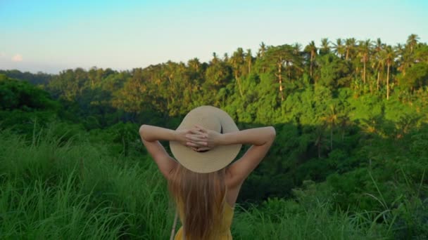 Filme super lento de uma jovem mulher em um vestido amarelo andando durante o pôr do sol no passeio de cume de Campuhan ou passarela de pintores em Ubud. Destinos Travell em Bali. Conceito de Travell para Bali . — Vídeo de Stock