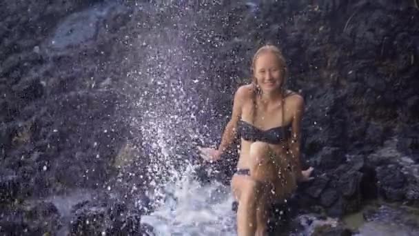 발리 섬의 화이트 샌드 비치 근처 화산 암석에서 자연이 만든 분수 또는 간헐천을 즐기는 젊은 여성의 슈퍼 슬로우 모션 샷 — 비디오