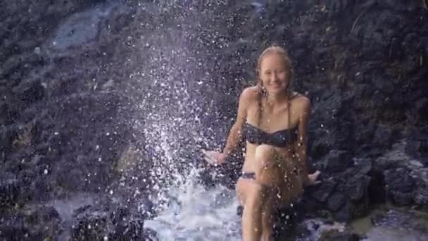 Superslowmotion disparo de una joven mujer disfrutando de las fuentes o géiseres hechos por la naturaleza en rocas volcánicas cerca de la playa de arena blanca en la isla de Bali — Vídeo de stock