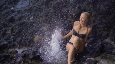 Bali adasında Beyaz kum plaj yakınındaki volkanik kayalar üzerinde doğa tarafından yapılan çeşmeler veya gayzerler zevk genç bir kadının Superslowmotion çekim
