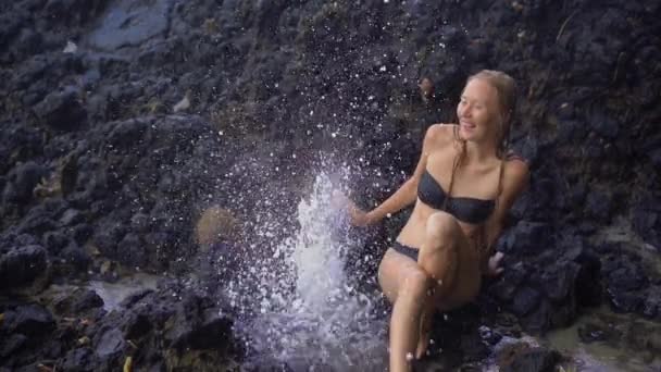 Superslowmotion tiro de uma jovem mulher apreciando as fontes ou gêiseres feitos por natureza em rochas vulcânicas perto da praia de areia branca na ilha de Bali — Vídeo de Stock