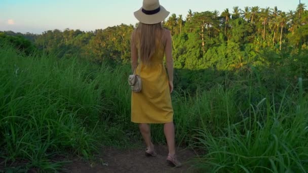 Super slowmotion shot of a young woman in a yellow dress walking during sunset at the Campuhan ridge walk or painters walkway in Ubud. Travell destinations on Bali. Travell to Bali concept. — Stock Video