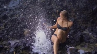 Bali adasında Beyaz kum plaj yakınındaki volkanik kayalar üzerinde doğa tarafından yapılan çeşmeler veya gayzerler zevk genç bir kadının Superslowmotion çekim