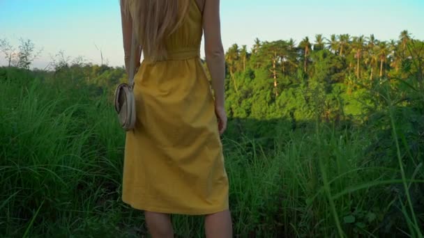 Super slowmotion shot of a young woman in a yellow dress walking during sunset at the Campuhan ridge walk or painters walkway in Ubud. Travell destinations on Bali. Travell to Bali concept. — Stock Video