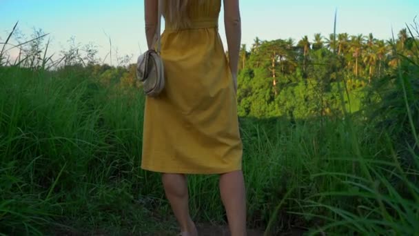 スーパースローモーションショットは、ウブドのカンプハンリッジウォークや画家の歩道で日没時に歩く黄色いドレスを着た若い女性のショット。バリ島の旅行先。バリのコンセプトへの旅. — ストック動画