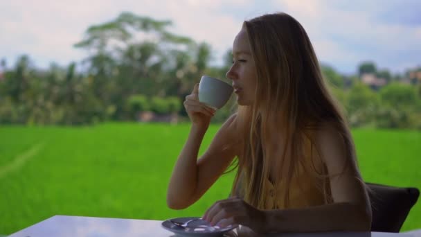 Closeup shot egy fiatal nő iszik teát vagy kávét egy vidéki kávézóban a rizs mező a háttérben — Stock videók