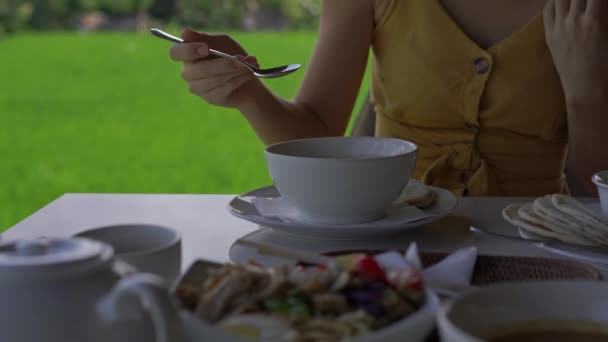 Nahaufnahme einer jungen Frau, die in einem Café mit einem Reisfeld im Hintergrund traditionelle ostasiatische Mahlzeiten genießt. Anreise zum bali concept. — Stockvideo